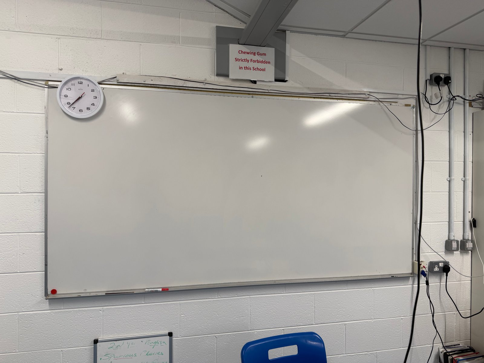 A classroom wall at Boherbue Comprehensive School with a whiteboard, a clock and a sign reading Chewing Gum Strictly Forbidden in this School